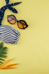Bikini and sunglasses decorate with bird of paradise flower and fern leaves on yellow background with copy space