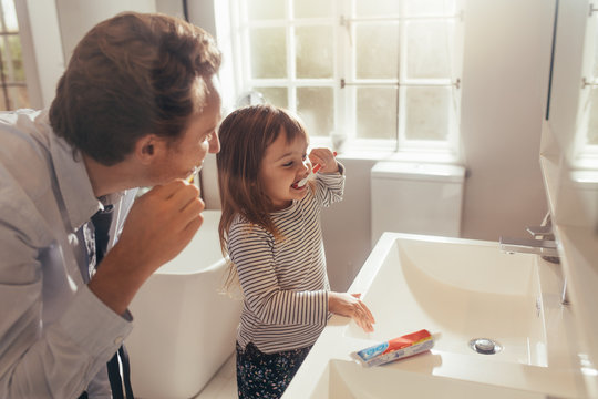 Father teaching daughter how to brush teeth