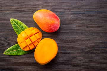 Fresh and beautiful mango fruit with sliced diced mango chunks on a dark wooden background, copy...