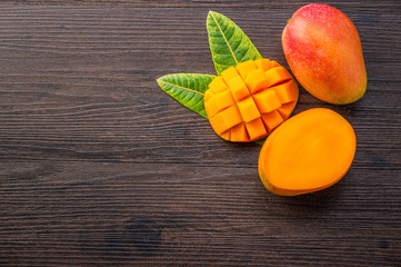 Fresh and beautiful mango fruit with sliced diced mango chunks on a dark wooden background, copy...
