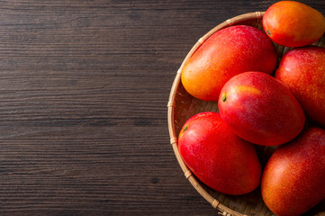 Fresh and beautiful mango fruit in a bamboo basket on a dark wooden background, copy space(text space), blank for text, top view.