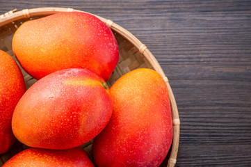 Fresh and beautiful mango fruit in a bamboo basket on a dark wooden background, copy space(text space), blank for text, top view.