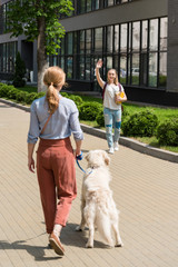 daughter waving to mother while she walking with dog on street