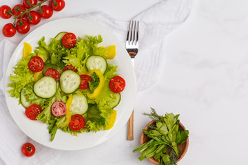 Green bright vegetable salad in a white plate on a white background, copy space, top view. A healthy vegetarian diet concept.
