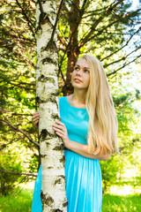 portrait Blonde russian woman hug birch. loong camera. summer forest. blue dress, natural