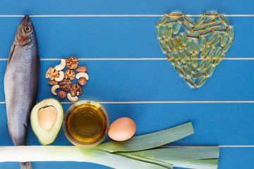 Selection of healthy food for heart and Cod liver fish oil supplements in a healthy heart shape on blue wooden dackground. Products rich in vitamin D: fish, olive oil, egg, avocado, nuts.