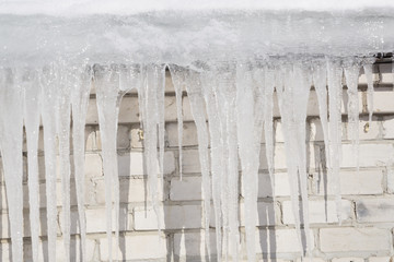 Wintry roof of the house with icicles on blue sky background.