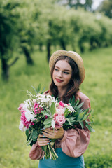 portrait of beautiful pensive woman in hat with bouquet of flowers in park