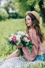 side view of beautiful pensive woman with bouquet of flowers resting on blanket in park