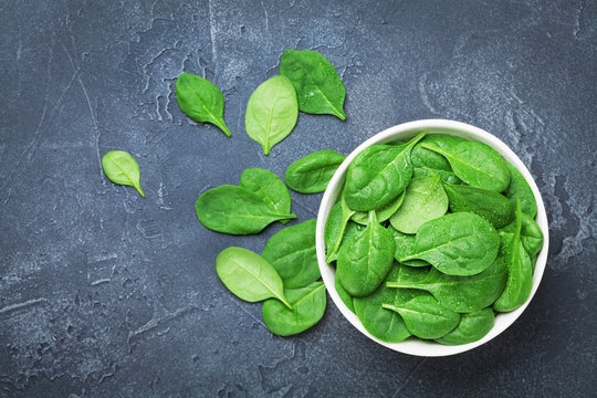 Green spinach leaves in bowl on black table top view. Organic and diet food.