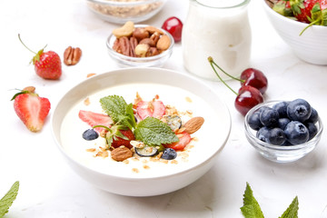 Serving option of granola bowl with mix of nuts, cereals, fruits and berries, greek yogurt. Healthy vegetarian breakfast, organic strawberry, blueberry, mint, almond. Close up, top view, background.