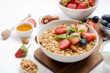 Serving option of granola bowl with mix of nuts, cereals, fruits and berries, greek yogurt. Healthy vegetarian breakfast, organic strawberry, blueberry, mint, almond. Close up, top view, background.