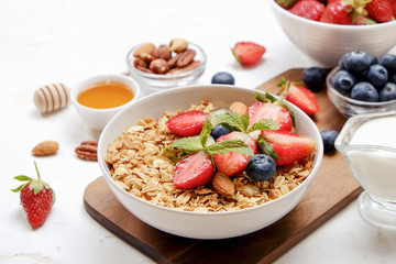 Serving option of granola bowl with mix of nuts, cereals, fruits and berries, greek yogurt. Healthy vegetarian breakfast, organic strawberry, blueberry, mint, almond. Close up, top view, background.