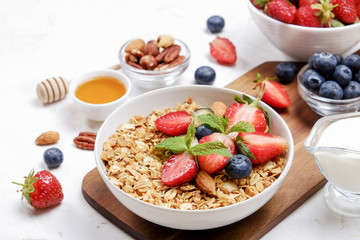 Serving option of granola bowl with mix of nuts, cereals, fruits and berries, greek yogurt. Healthy vegetarian breakfast, organic strawberry, blueberry, mint, almond. Close up, top view, background.