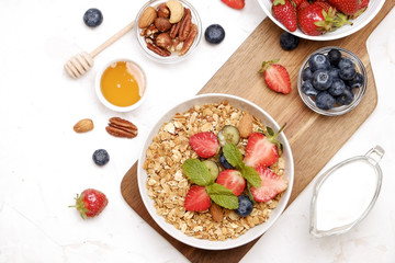 Serving option of granola bowl with mix of nuts, cereals, fruits and berries, greek yogurt. Healthy vegetarian breakfast, organic strawberry, blueberry, mint, almond. Close up, top view, background.