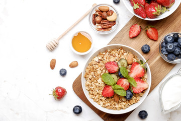 Serving option of granola bowl with mix of nuts, cereals, fruits and berries, greek yogurt. Healthy vegetarian breakfast, organic strawberry, blueberry, mint, almond. Close up, top view, background.