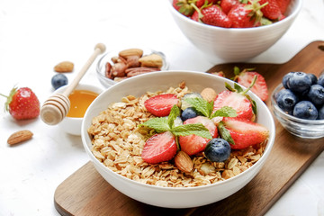Serving option of granola bowl with mix of nuts, cereals, fruits and berries, greek yogurt. Healthy vegetarian breakfast, organic strawberry, blueberry, mint, almond. Close up, top view, background.