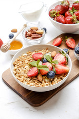 Serving option of granola bowl with mix of nuts, cereals, fruits and berries, greek yogurt. Healthy vegetarian breakfast, organic strawberry, blueberry, mint, almond. Close up, top view, background.