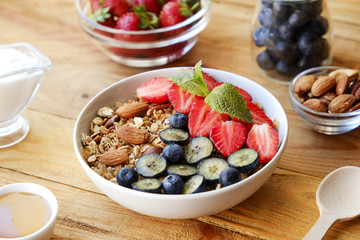 Serving option of granola bowl with mix of nuts, cereals, fruits and berries, greek yogurt. Healthy vegetarian breakfast, organic strawberry, blueberry, mint, almond. Close up, top view, background.