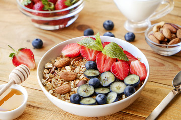 Serving option of granola bowl with mix of nuts, cereals, fruits and berries, greek yogurt. Healthy vegetarian breakfast, organic strawberry, blueberry, mint, almond. Close up, top view, background.