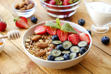 Serving option of granola bowl with mix of nuts, cereals, fruits and berries, greek yogurt. Healthy vegetarian breakfast, organic strawberry, blueberry, mint, almond. Close up, top view, background.