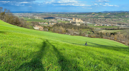 green landscape on hills around Parma with lonely person sitting in grass field near Torrechiara castle,  Italy