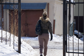 back of a young girl dressed in leather jacket with brown leather backpack on white .