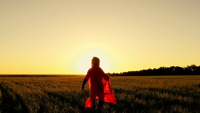 Superhero runs on a green lawn against the backdrop of a sunset pretending to be flying, in slow motion
