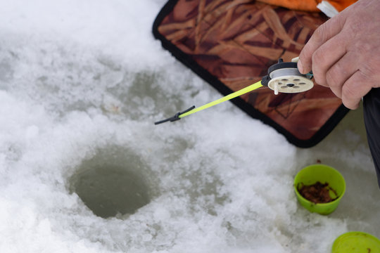 Fishing by a winter plastic rod in the ice hole on the pond .