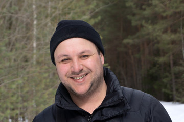 An attractive forty something man with long curly hair poses for a photo while out for a walk in the woods in winter.