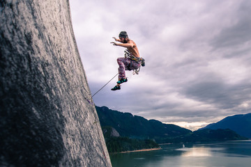 Man with climbing rope jumping off rock face on Malamute, Squamish, Canada