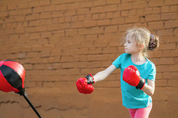 Little girl strongly and emotionally hits the punching bag. Selective focus