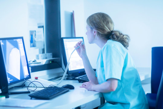 Radiologist communicating with patient through microphone, watching computer screens in control room