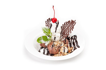 The ball of chocolate ice cream and the shaken up cream powdered with icing sugar on a white dish, are decorated by berries and nuts, watered with chockolate jam. It is isolated on a white background.