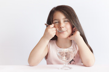 Happy child girl eating ice cream in white and chocolate bowl on white background. Enjoying delicious.