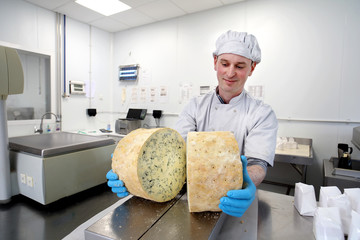 Cheese maker inspecting mould inside large cut wheel of stilton
