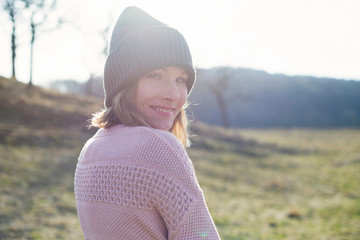 Sunlit portrait of mid adult woman in sunlit field looking over her shoulder