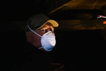 Man in dust mask looking sideways from dark loft, portrait