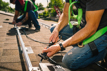 Two workmen installing solar panels on roof of house, mid section