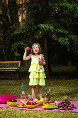 little girl in a dress throws a bubble at a picnic in a summer forest