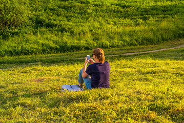 Girl looking at smartphone sitting on green hill