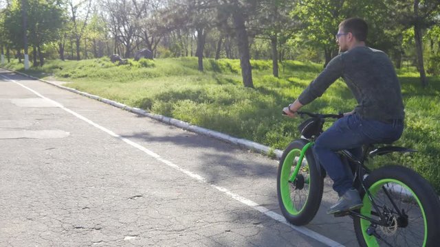 Man rides pedals Electric bicycle in a green park on asphalt trail
