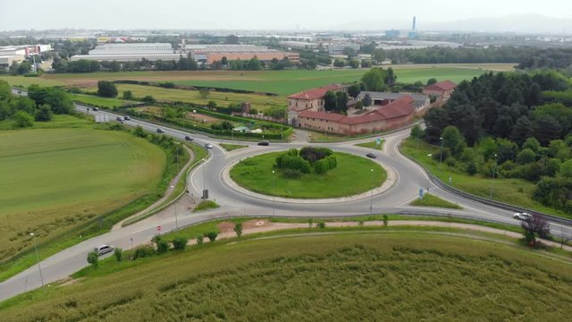 Aerial: traffic circle in suburban outskirt, roundabout in the green countryside, cars driving