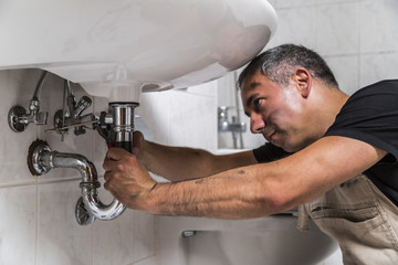 specialist male plumber repairs faucet in bathroom