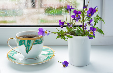 Wild flowers pansies and a Cup of coffee on the windowsill in rainy weather