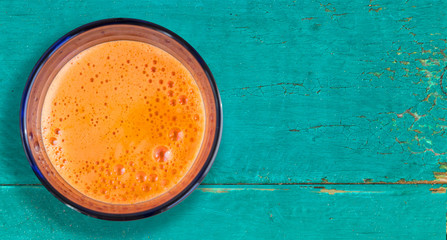 Carrot juice - colorful healthy drink in glass on old blue wooden table. Top view.. Copy space.