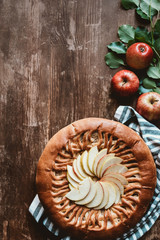 top view of arranged apple pie and fresh apples with green leaves on wooden surface