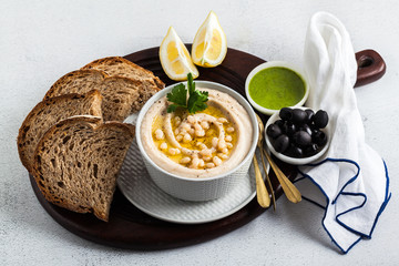 hummus of white cannellini beans, served with arugula pesto and rye bread, olives and lemon on a table