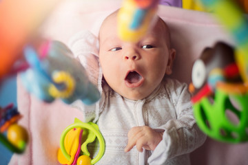 Cute little infant baby newborn playing with toys on colorful mat; sunflare; early development concept; top view