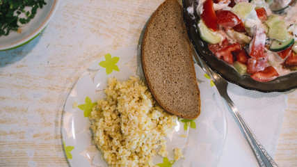 Homemade authentic russian ukrainian summer lunch at country side; salad with tomatoes and cucumbers and sour cream; porridge, baked chicken ; rural Eastern Europe